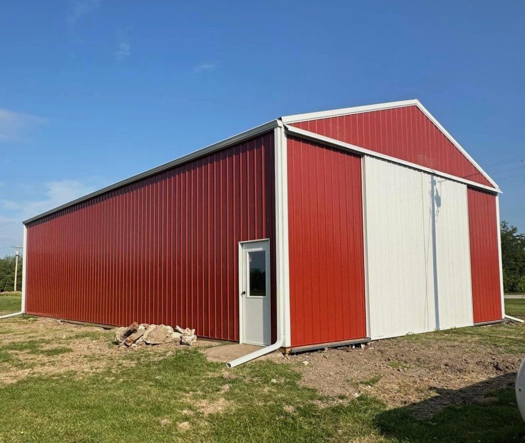 Red and white pole barn under construction in a rural area, featuring post-frame construction for cost-effective, versatile storage or workshop use.