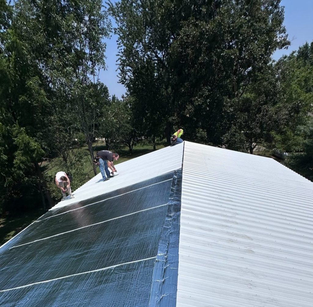 Workers installing reflective insulation on a metal roof in preparation for mounting solar photovoltaic panels.